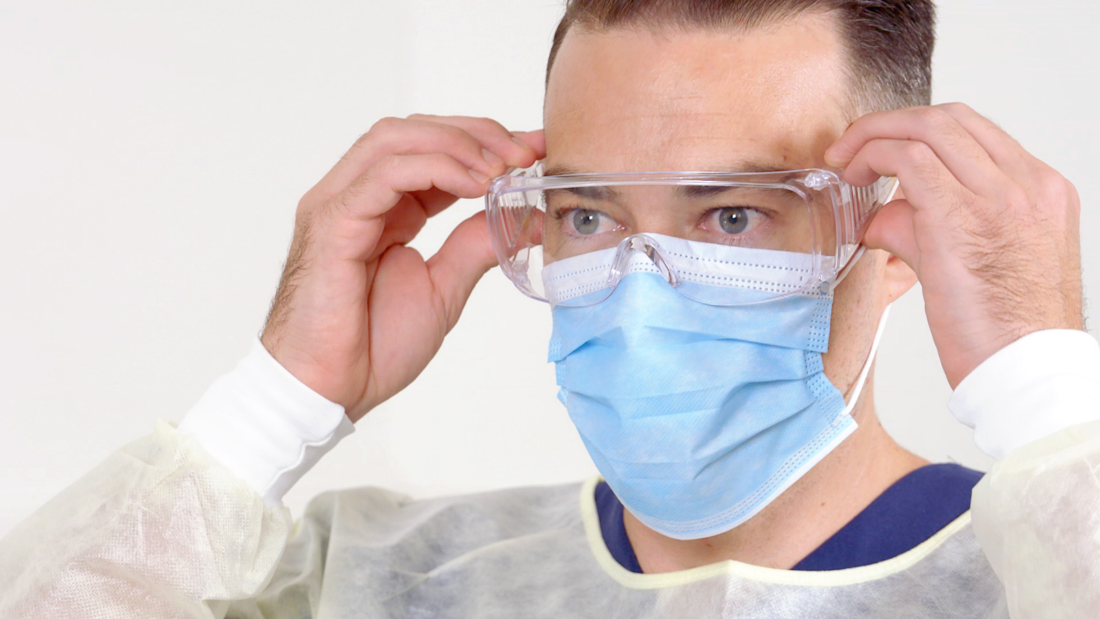 A man in personal protective equipment adjusts his safety glasses